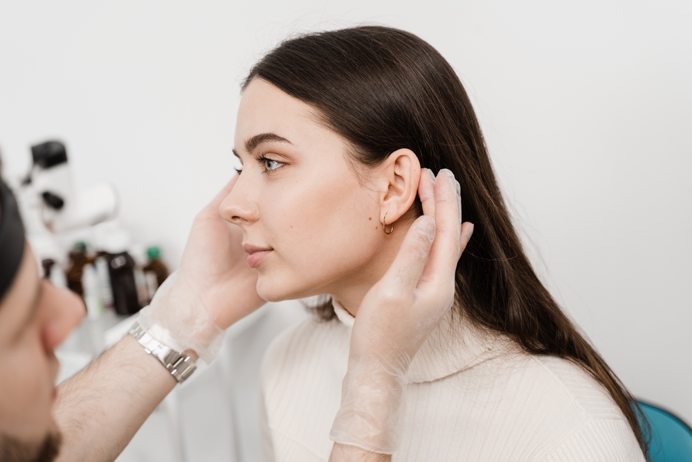 Doctor looking at woman's ears before otoplasty in Andover, MA