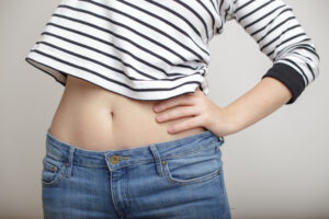 Woman in jeans showing her slim, tight abs after a tummy tuck in Andover, MA